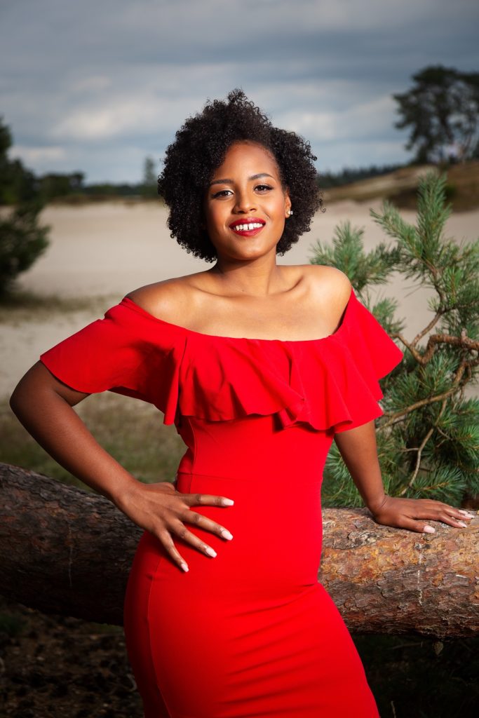 African woman posing on tree trunk wearing red dress and red lipstick